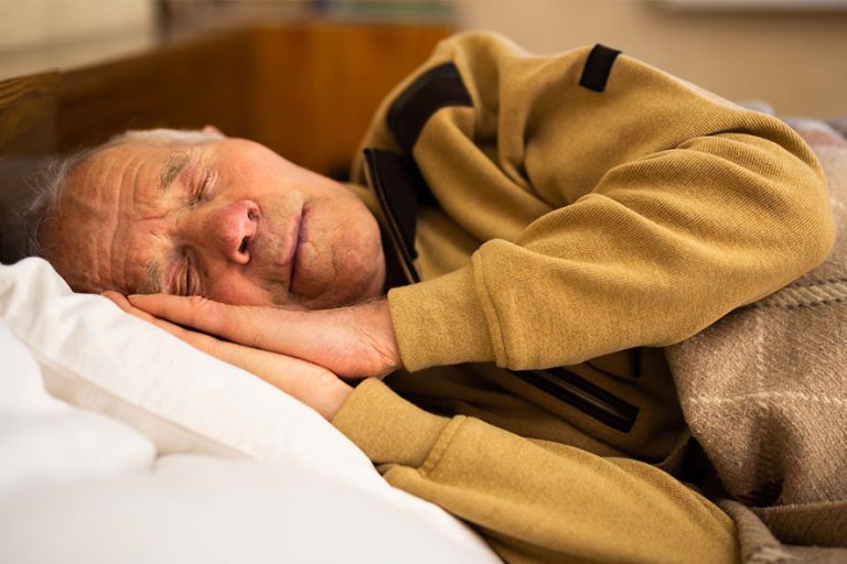 Älterer Mann schläft seitlich auf seinen Händen und trägt gelbes Sweatshirt