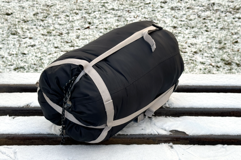 Schwarzer Schlafsack die auf einer Bank liegt, die mit Schnee bedeckt ist