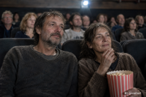 Mann und Frau um die 50 sitzen in einem Kinosaal und schauen einen Film, sie essen dabei Popcorn.